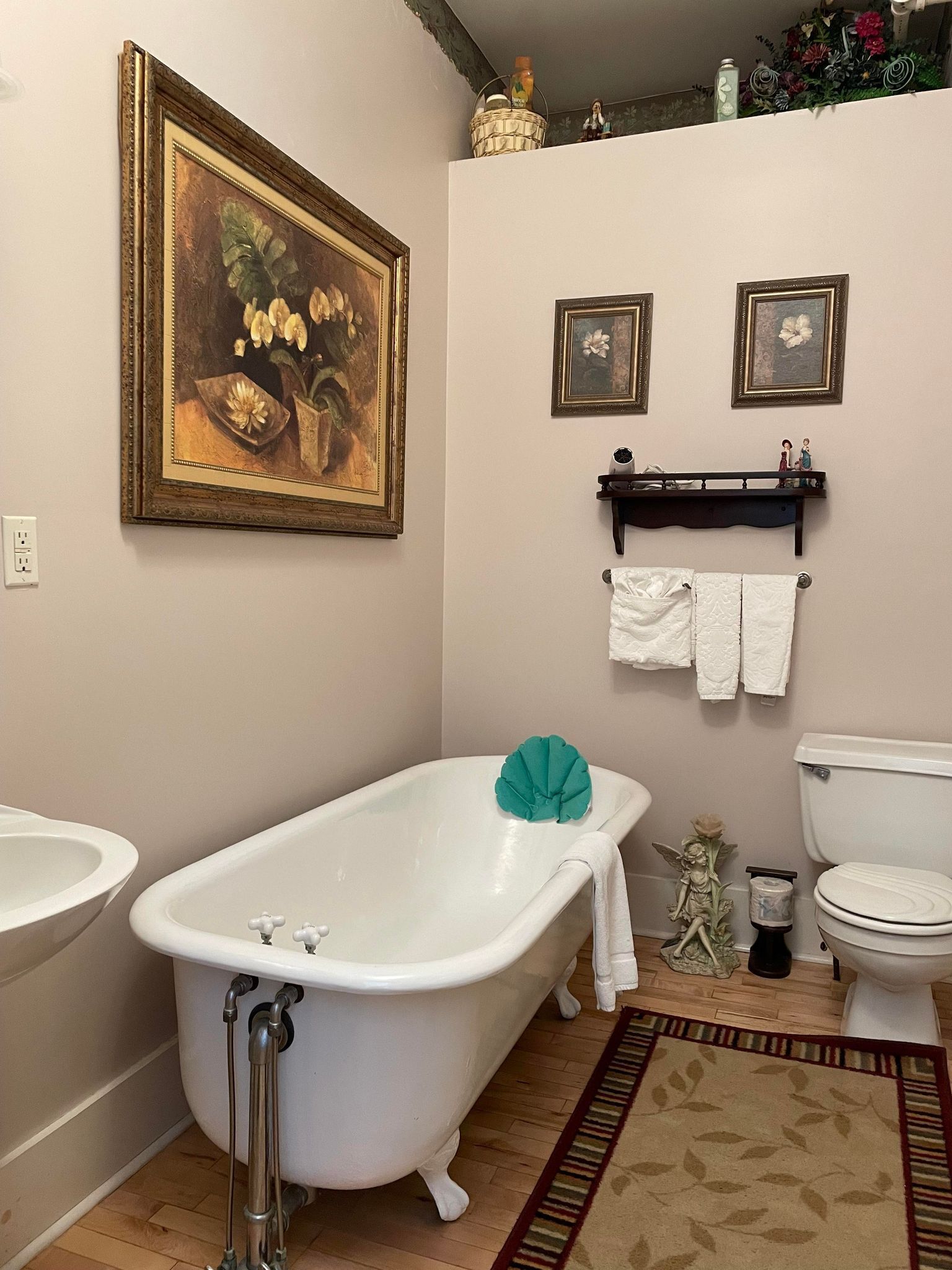 A bathroom with a clawfoot bathtub, a toilet, a sink, and a framed floral painting on the wall.