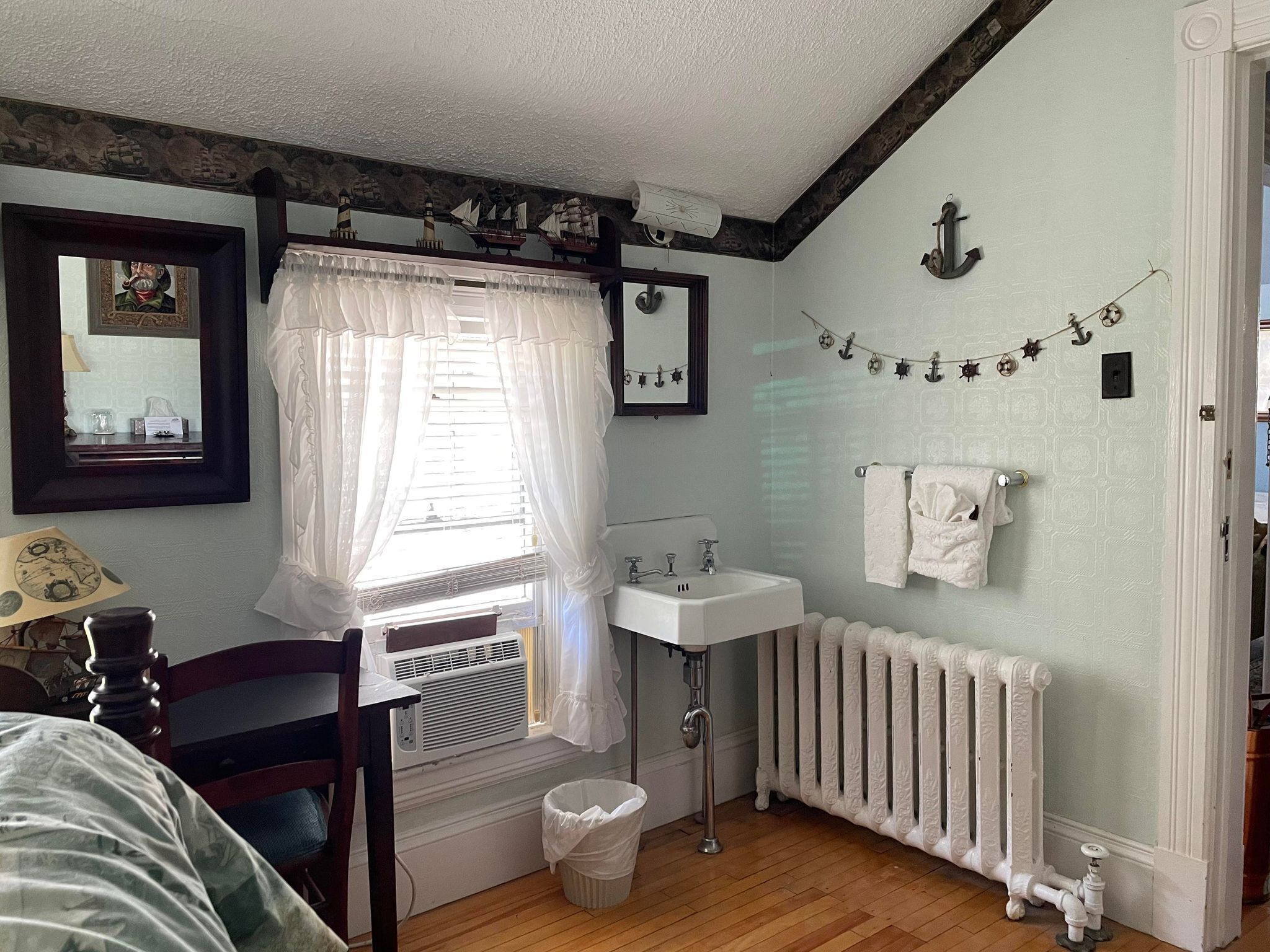 Un baño con lavamanos blanco, radiador, espejo y ventana con cortina.
