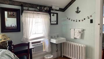 Un baño con lavamanos blanco, radiador, espejo y ventana con cortina.
