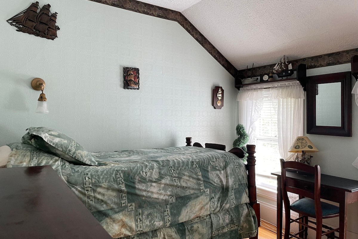 Un dormitorio con cama, escritorio, silla, reloj y ventana con cortinas.