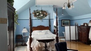 A bedroom with a four-poster bed, a chandelier, a wooden dresser, and a chair. - Marshlands Inn (Sackville)