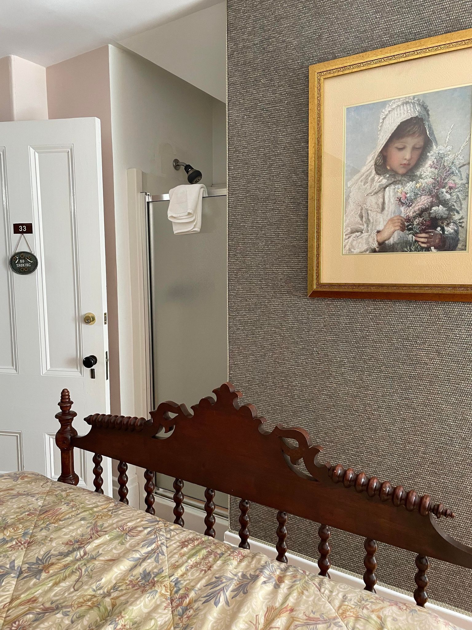A bedroom with a wooden headboard, a framed picture on the wall, and a door with a 'no smoking' sign.