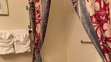 A bathroom with a bathtub, a shower curtain with a floral pattern, a towel rack with towels, and a handrail.