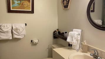 A bathroom with a toilet, sink, and towel rack. There is a framed picture on the wall and a mirror with lights.