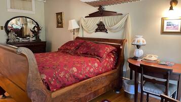 A traditional bedroom with a wooden bed, a bedside table with a lamp, a mirror, and a framed picture on the wall.