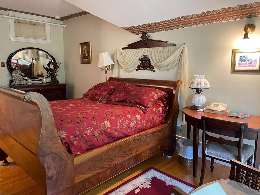 A traditional bedroom with a wooden bed, a bedside table with a lamp, a mirror, and a framed picture on the wall.