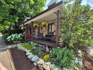 Un edificio de piedra con un porche cubierto, mobiliario exterior y un jardín con diversas plantas y flores.