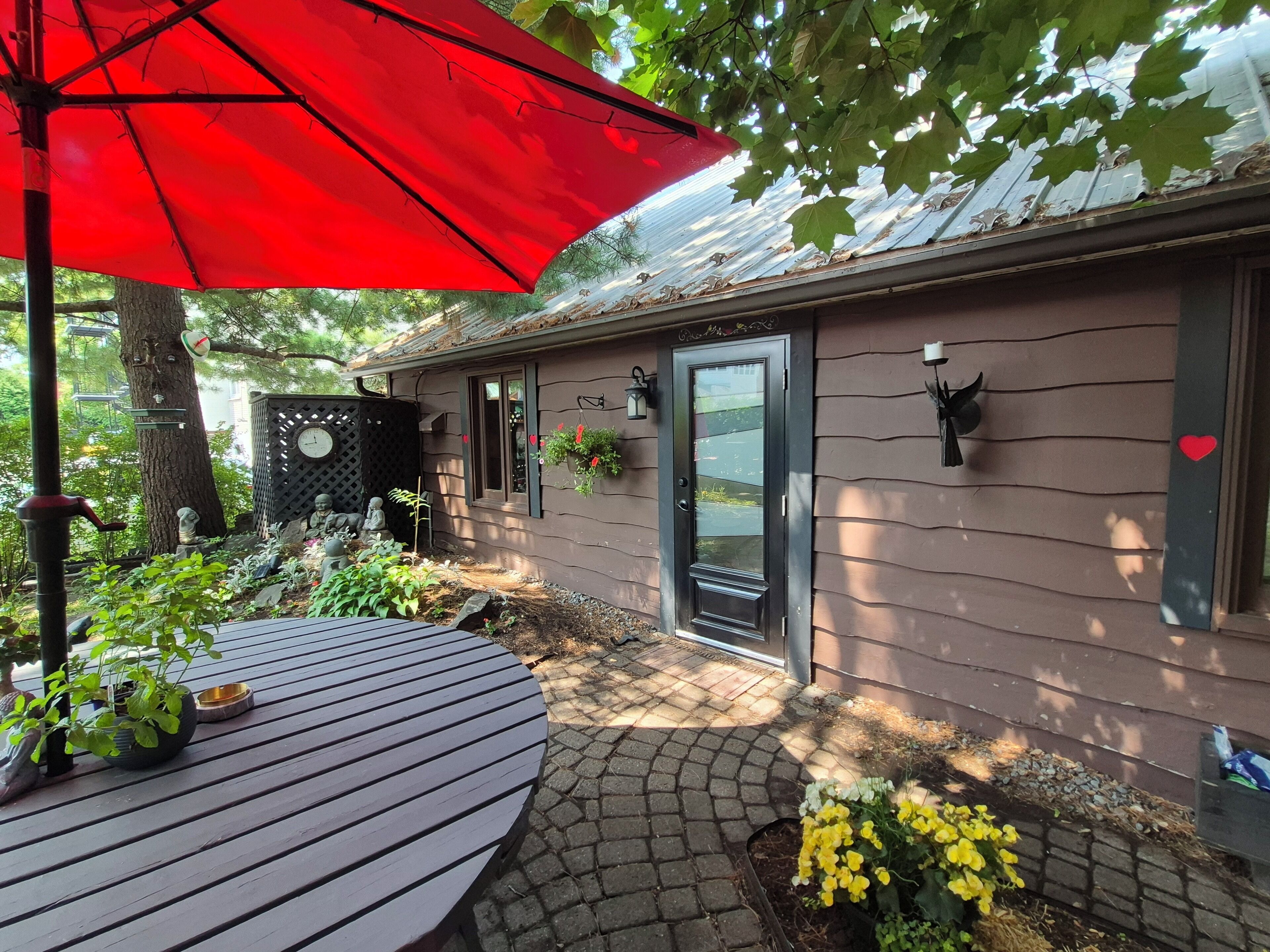 A patio area with a round wooden table, a red umbrella, and potted plants.