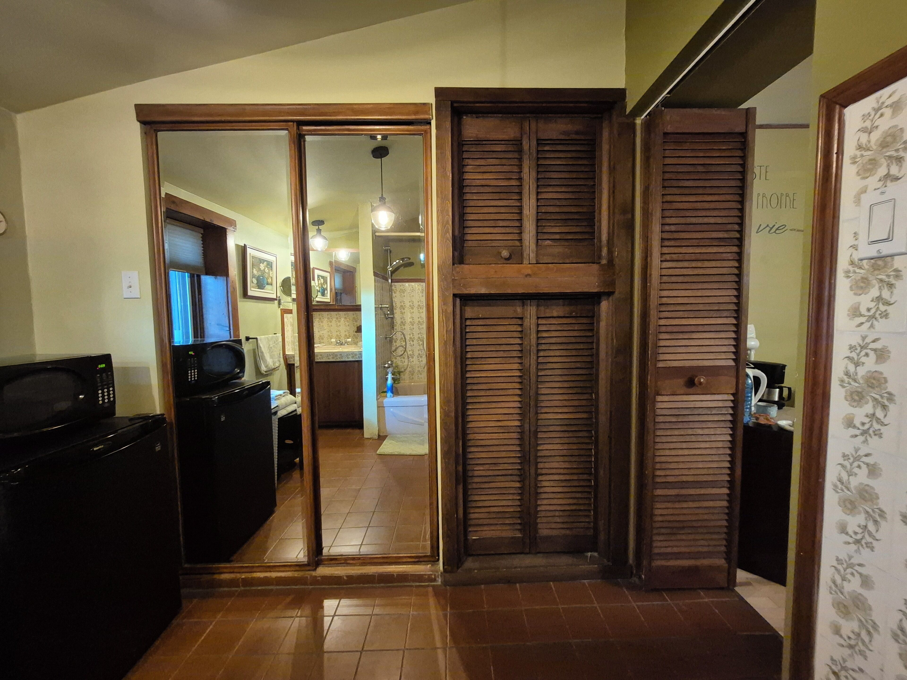 Una cocina con microondas, refrigerador y pileta. Hay una puerta de madera que da a un baño con ducha y retrete.
