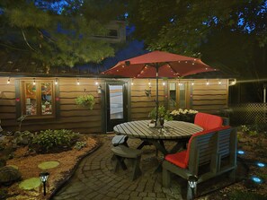 Un patio con mesa y sillas, una planta colgante y luces decorativas.