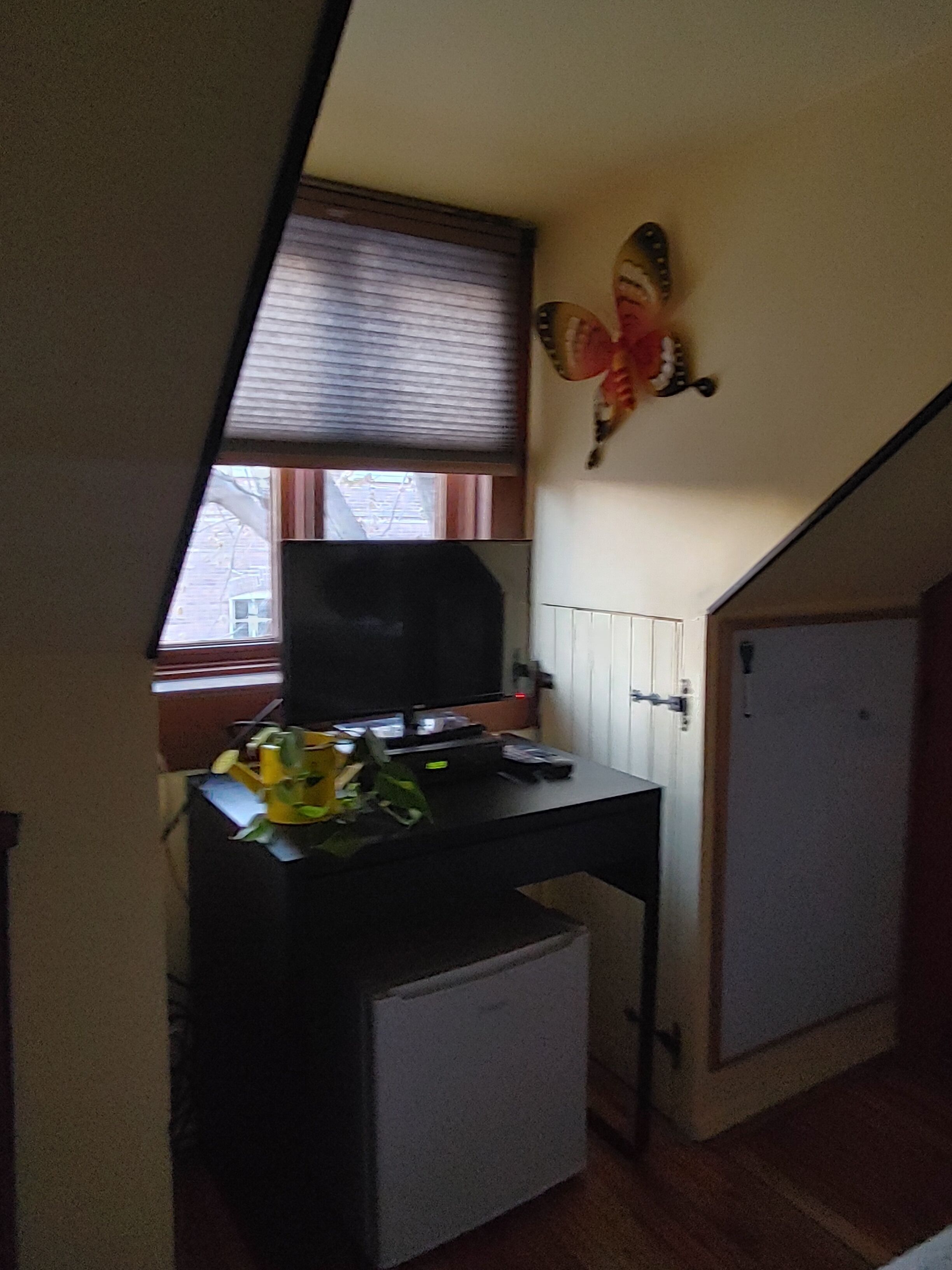 Une pièce de taille modeste, comprenant un petit bureau, un radiateur et une fenêtre équipée de stores.