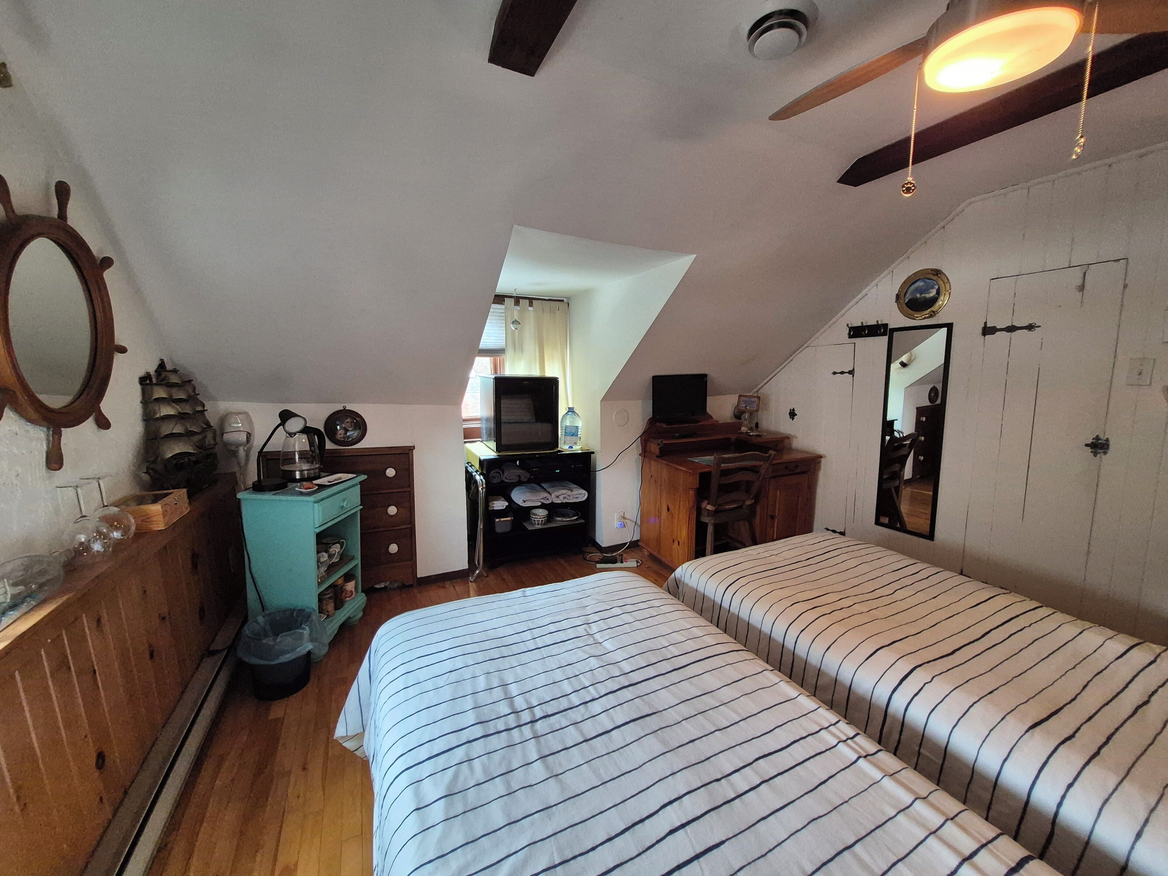 A bedroom with two beds, a desk, a chair, a mirror, and a ceiling fan.