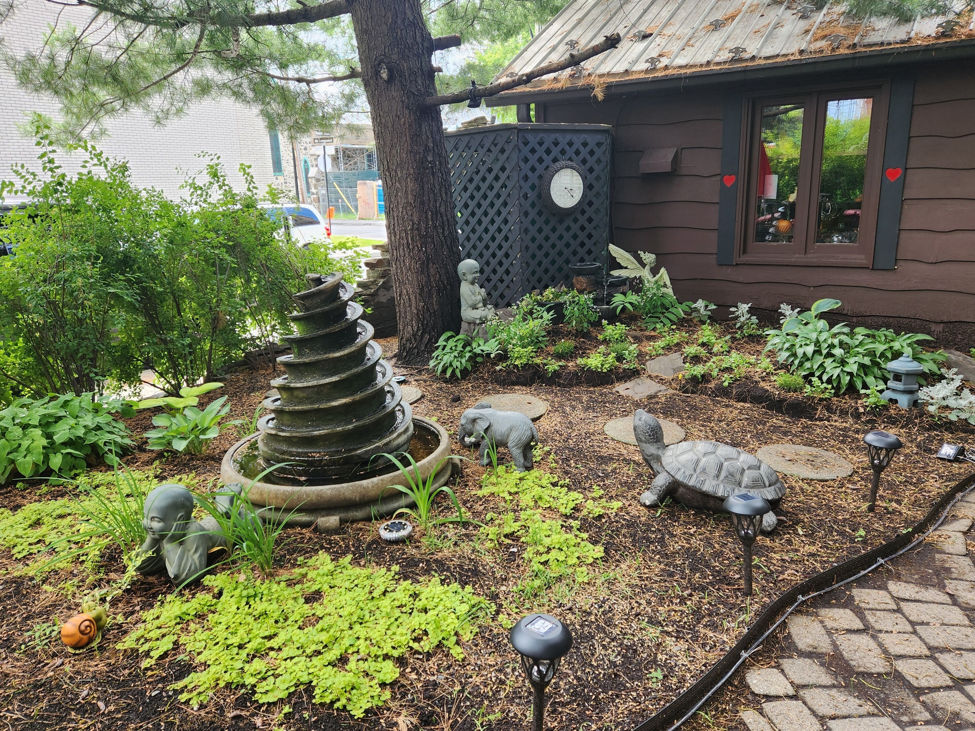 A garden with a spiral stone structure, various plants, and garden statues.