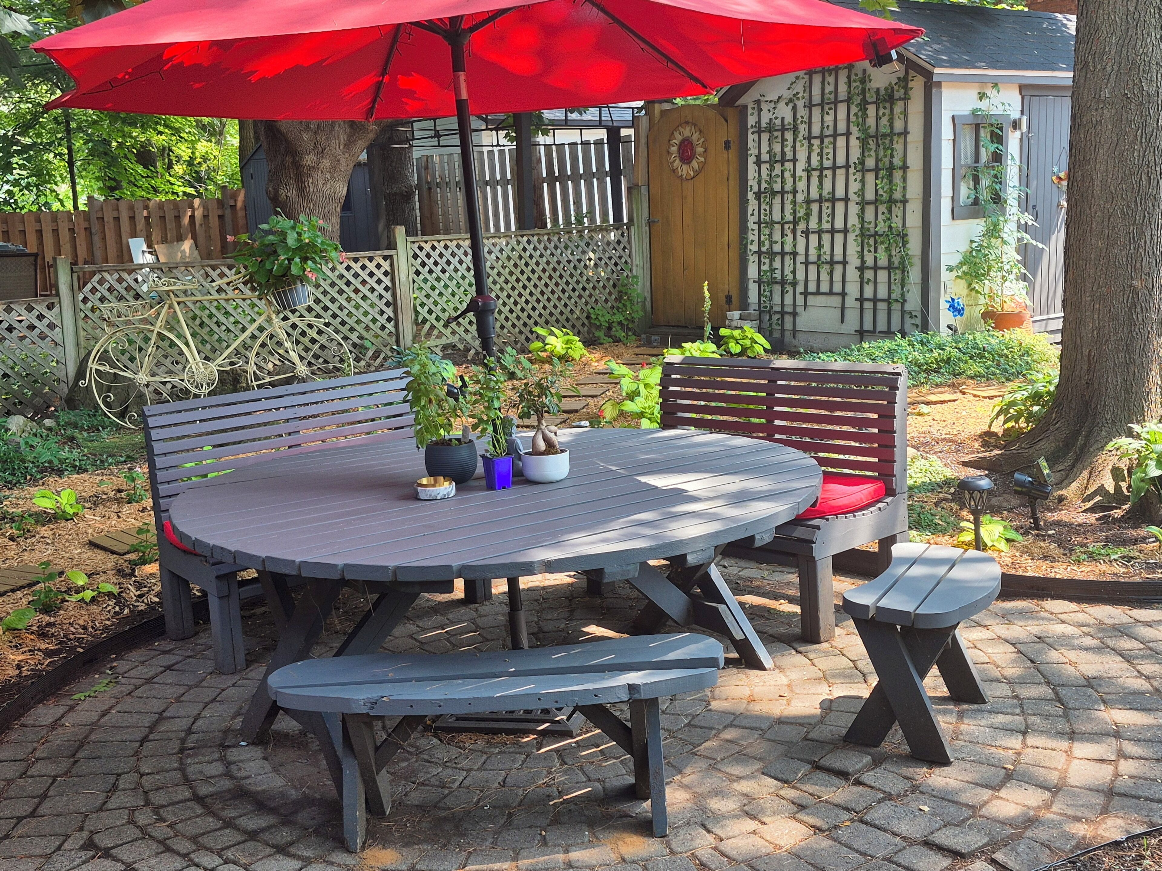 A patio with a round table, benches, and a red umbrella.