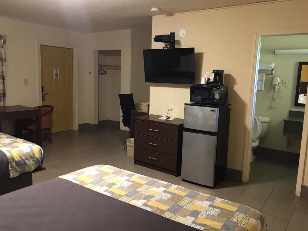A hotel room with a bed, a desk, a dresser, a microwave, and a television.