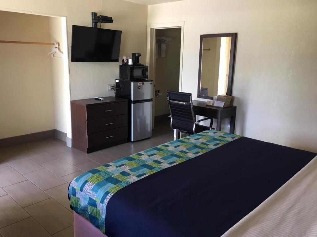 A hotel room with a bed, a desk, a chair, a television, a microwave, and a refrigerator.