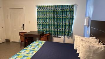 A hotel room with a bed, a desk, a chair, a window with curtains, and a radiator.