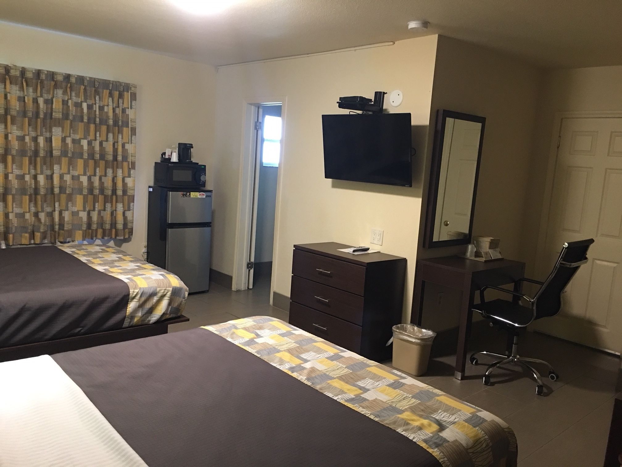 Ein Hotelzimmer mit zwei Betten, einem Schreibtisch, einem Sessel, einem Fernseher, einer Mikrowelle und einem Kühlschrank.