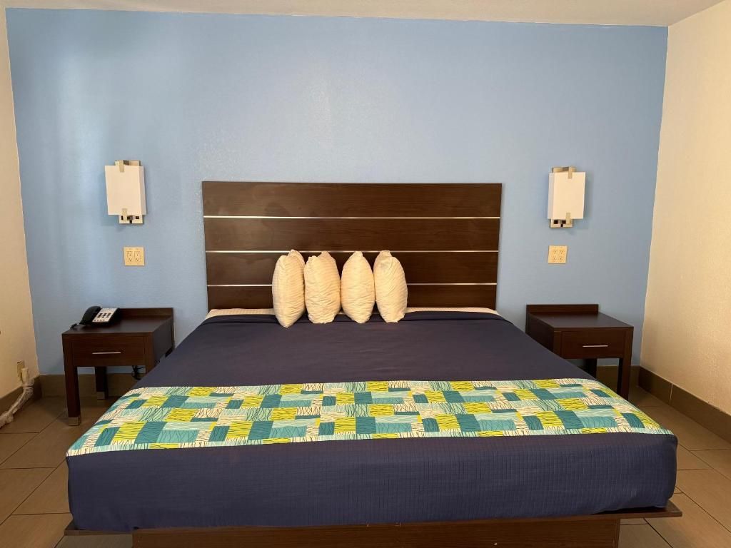 A hotel room with a large bed, a headboard with multiple pillows, bedside tables, and wall-mounted lamps.