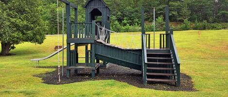 A playground with a slide, climbing area, and a small covered structure.
