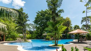 A swimming pool with a curved edge, surrounded by lush greenery and a thatched-roof structure. - Laguna Lodge (Colorado)
