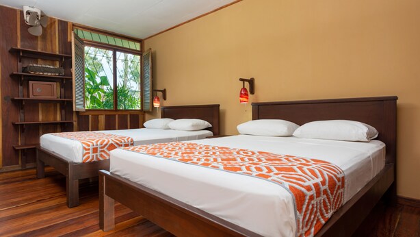 A hotel room with two wooden beds, a window with blinds, a shelf unit, and a wall-mounted lamp. - Laguna Lodge (Colorado)