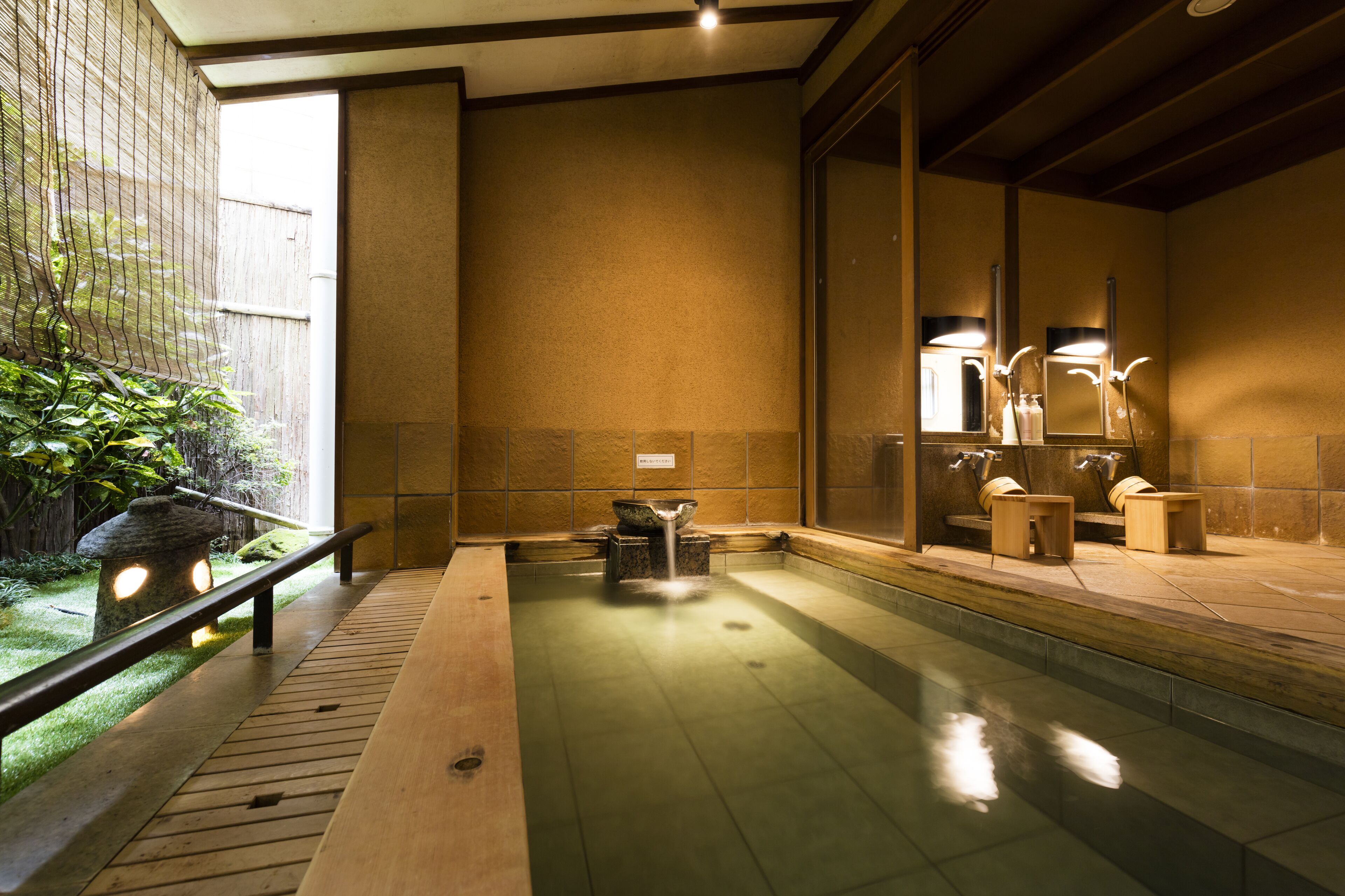 Un onsen japonés tradicional con un banco de madera, una cuenca de piedra y una pequeña cascada.