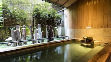 Un onsen japonais traditionnel, avec un intérieur en bois, un bain en pierre et une vue sur la verdure par une fenêtre.
