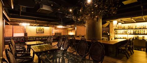 Un restaurante con varias mesas y sillas, una zona de bar con botellas y una planta decorativa.