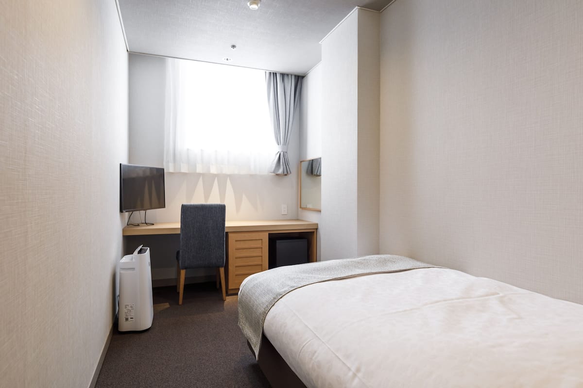 Ett hotellrum med en säng, ett skrivbord, en stol, en dator och ett litet bord.