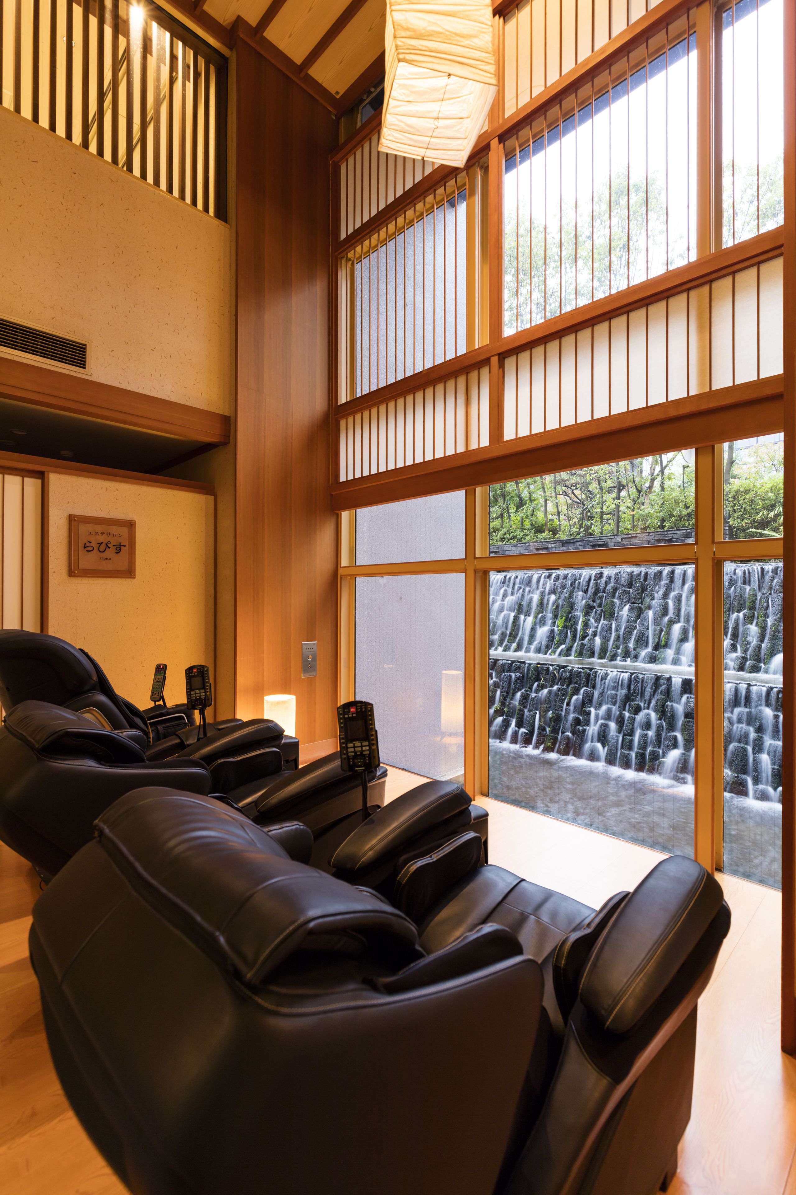Een massageruimte met zwarte massagestoelen, een houten plafond en uitzicht op een waterval.