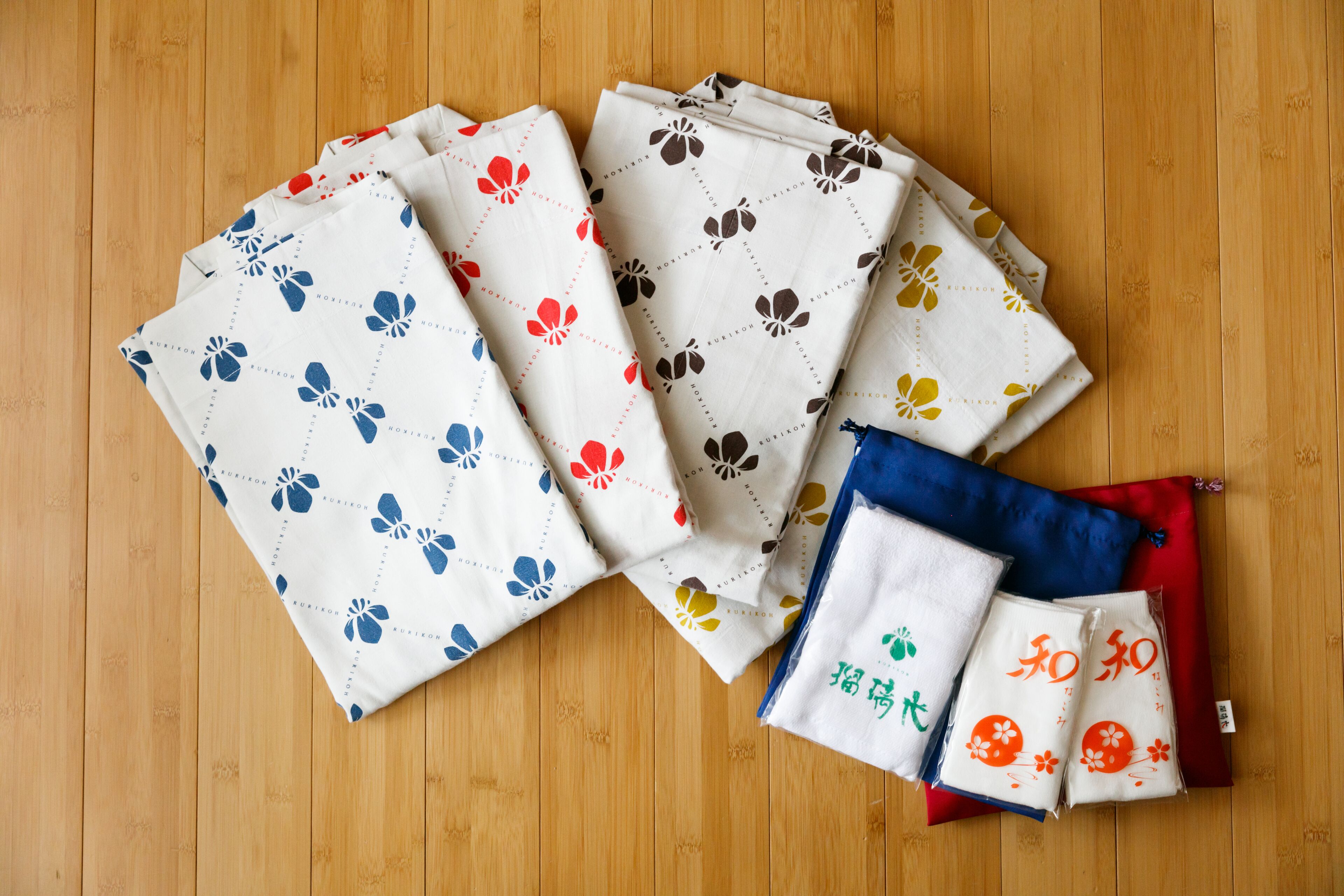 A variety of folded textiles with floral patterns on a wooden floor.