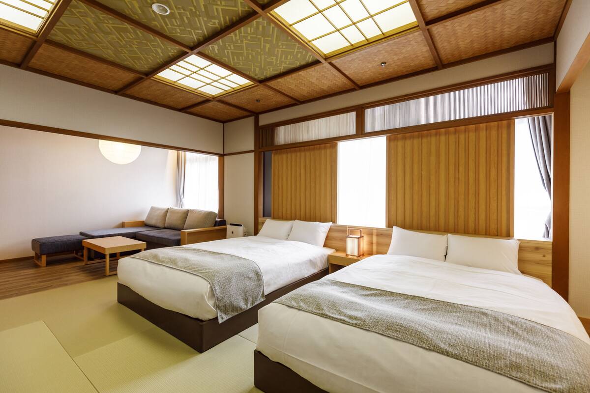 Ett traditionellt japanskt rum med tatamimattor på golvet, två sängar med vitt sänglinne, ett lågt träbord och en soffa.