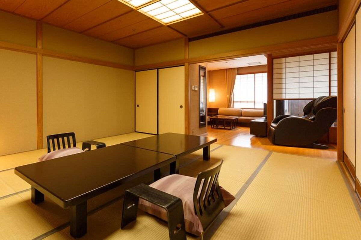A traditional Japanese room with tatami flooring, a low table, chairs, a sofa, and a massage chair.