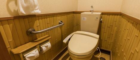 A small, compact bathroom with a toilet, a handrail, and a towel hanging on the wall.