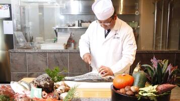 A chef in a white uniform preparing food in a kitchen with stainless steel appliances and a tiled backsplash.