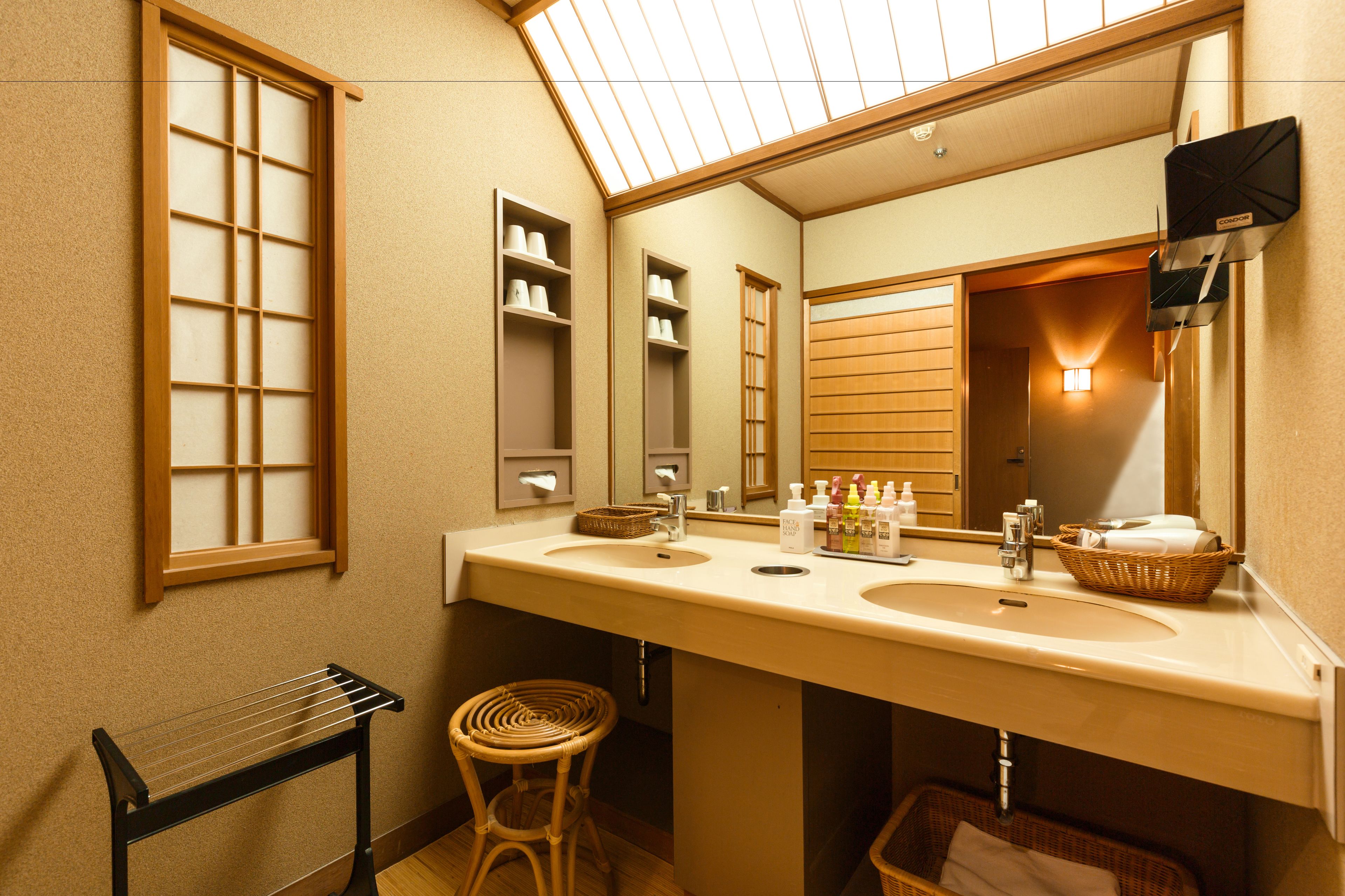 Une salle de bain avec deux lavabos, un grand miroir, un porte-serviettes et un tabouret en osier.