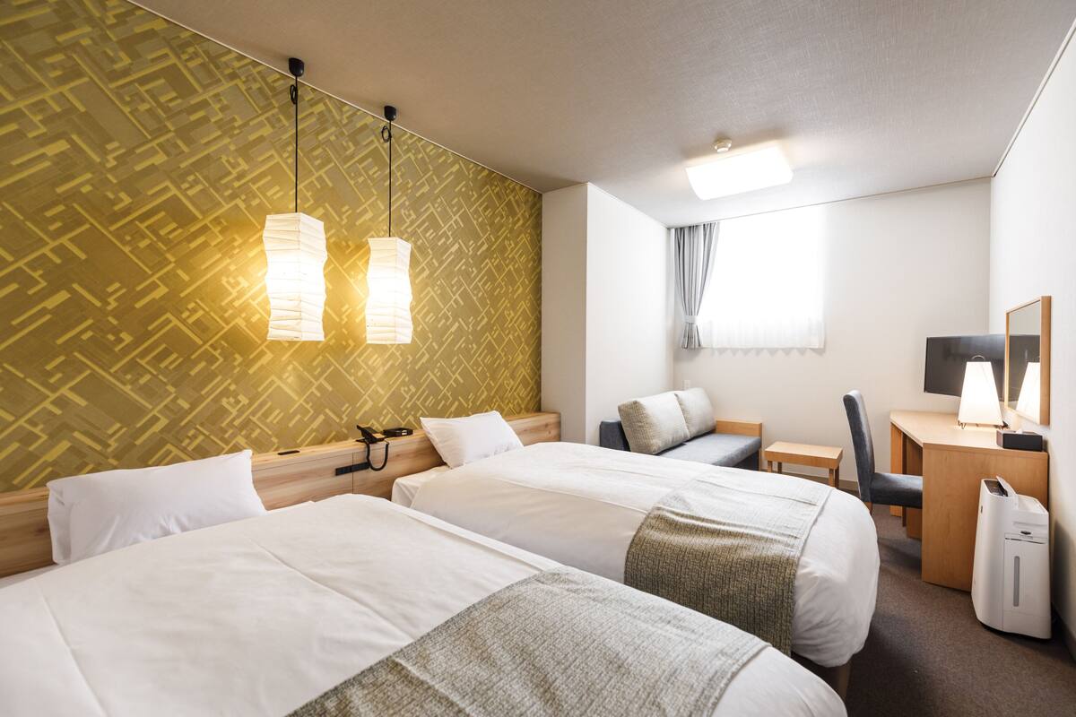 Ett hotellrum med två sängar, ett skrivbord, en stol, en lampa och en spegel.