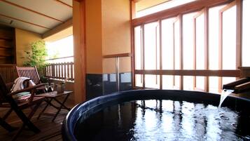 A hot tub with water flowing, wooden deck chairs, and a view through large windows.