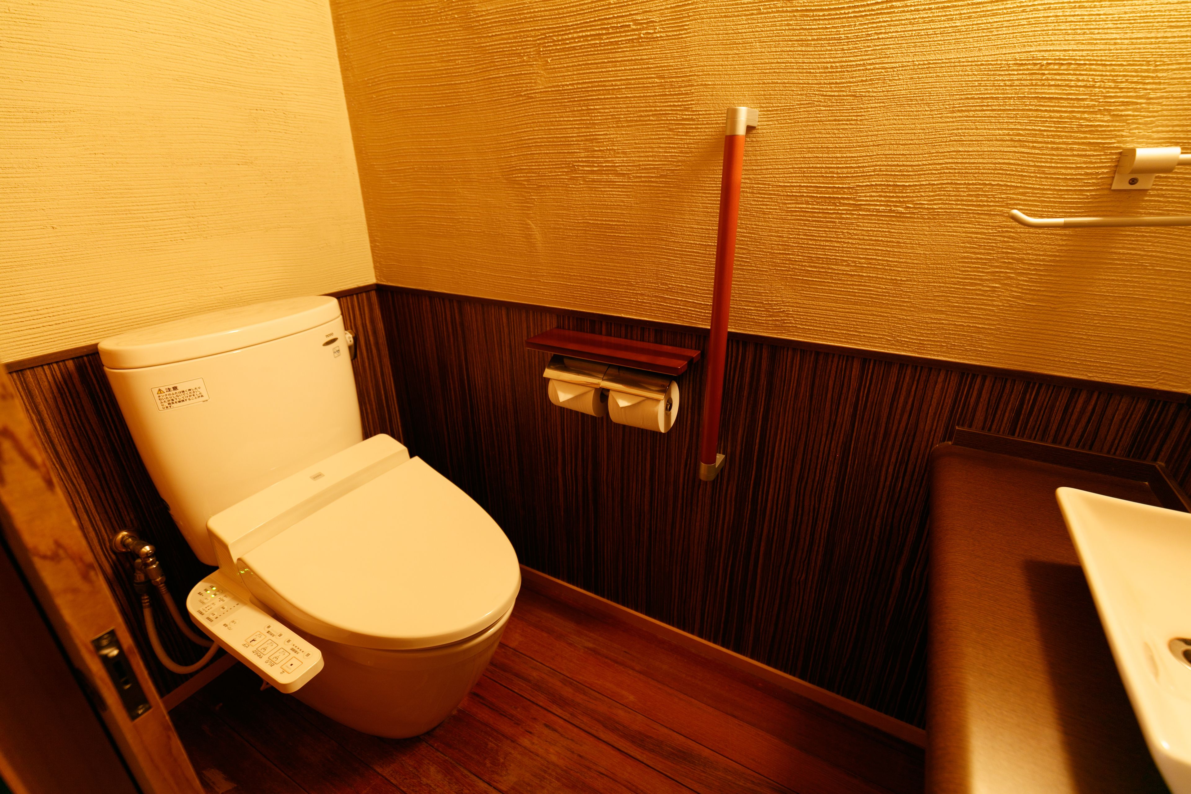 A small, compact bathroom with a wooden floor, a white toilet, and a wooden vanity with a sink.