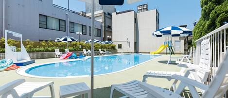 Piscina con sillas de descanso y sombrillas, rodeada de edificios.