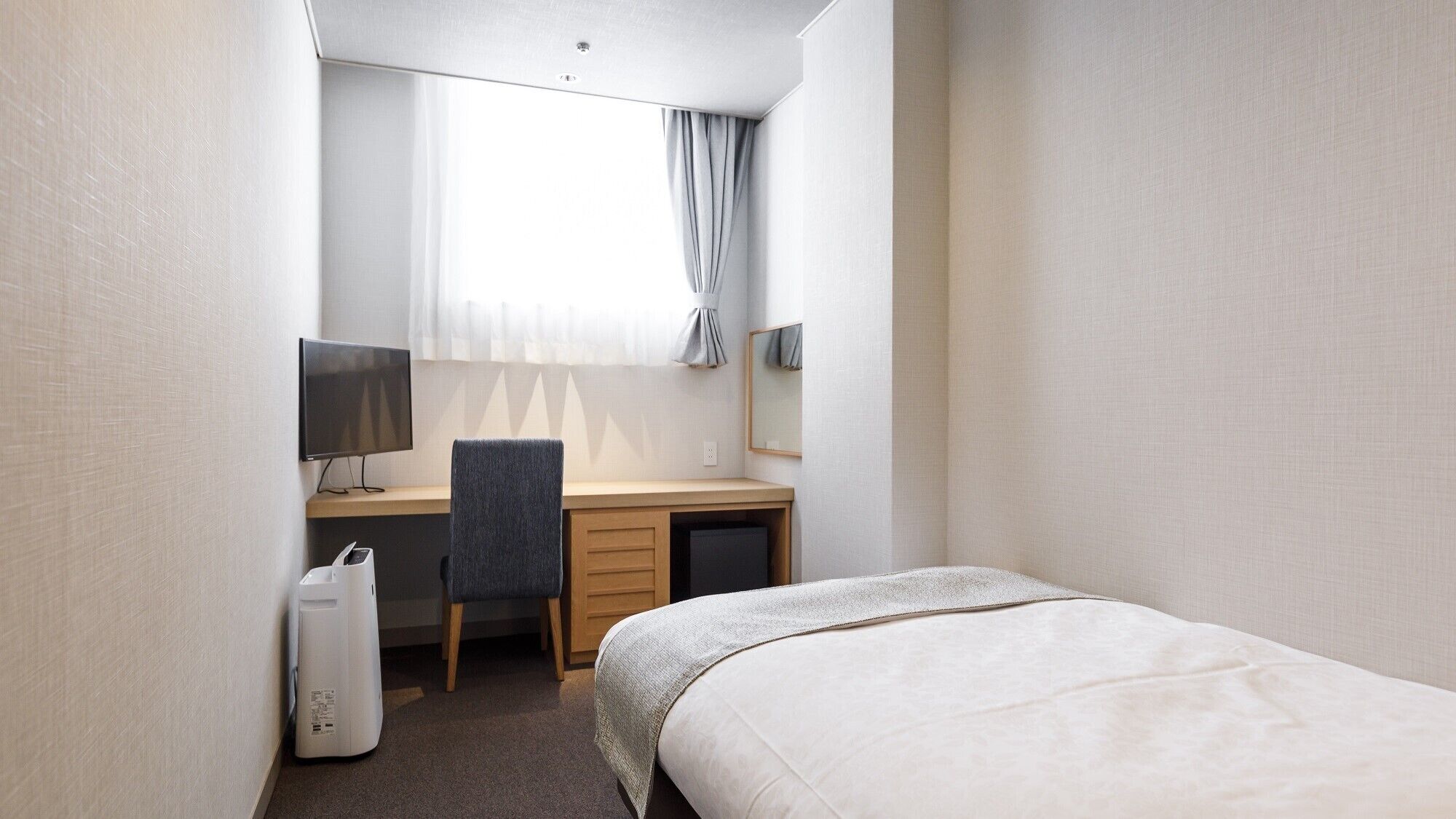 A hotel room with a bed, a desk with a chair, a television, and a window with curtains.