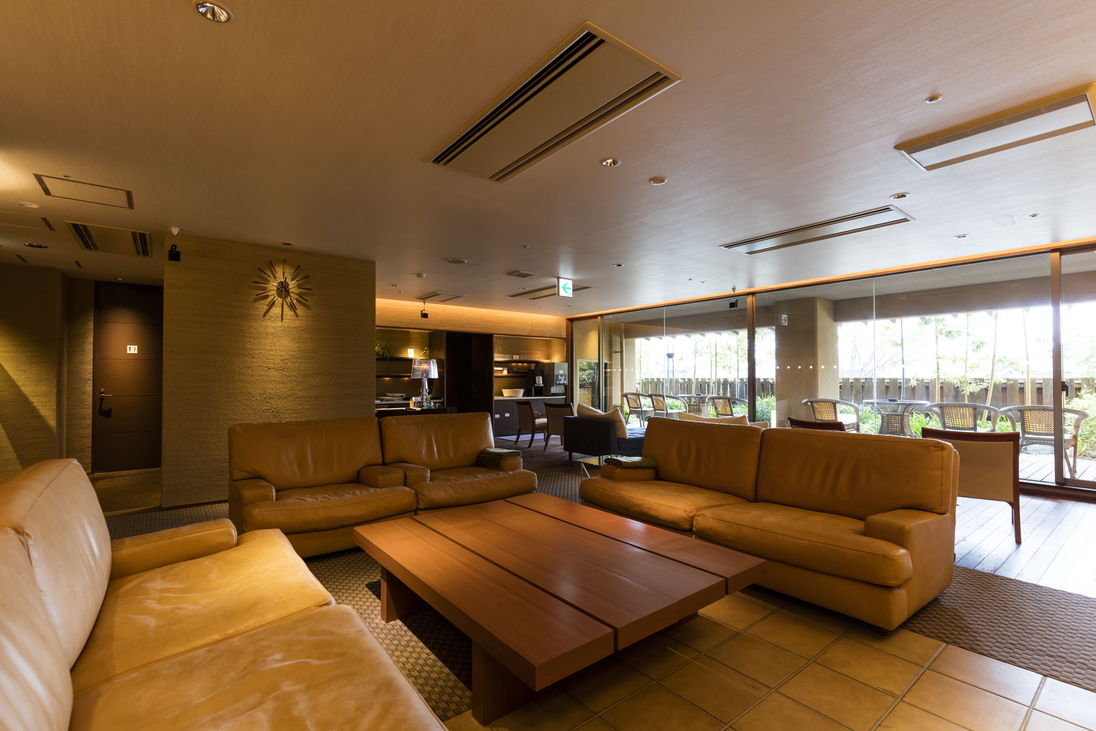 A modern hotel lobby with leather sofas, a wooden coffee table, and large windows offering a view of the outdoors.