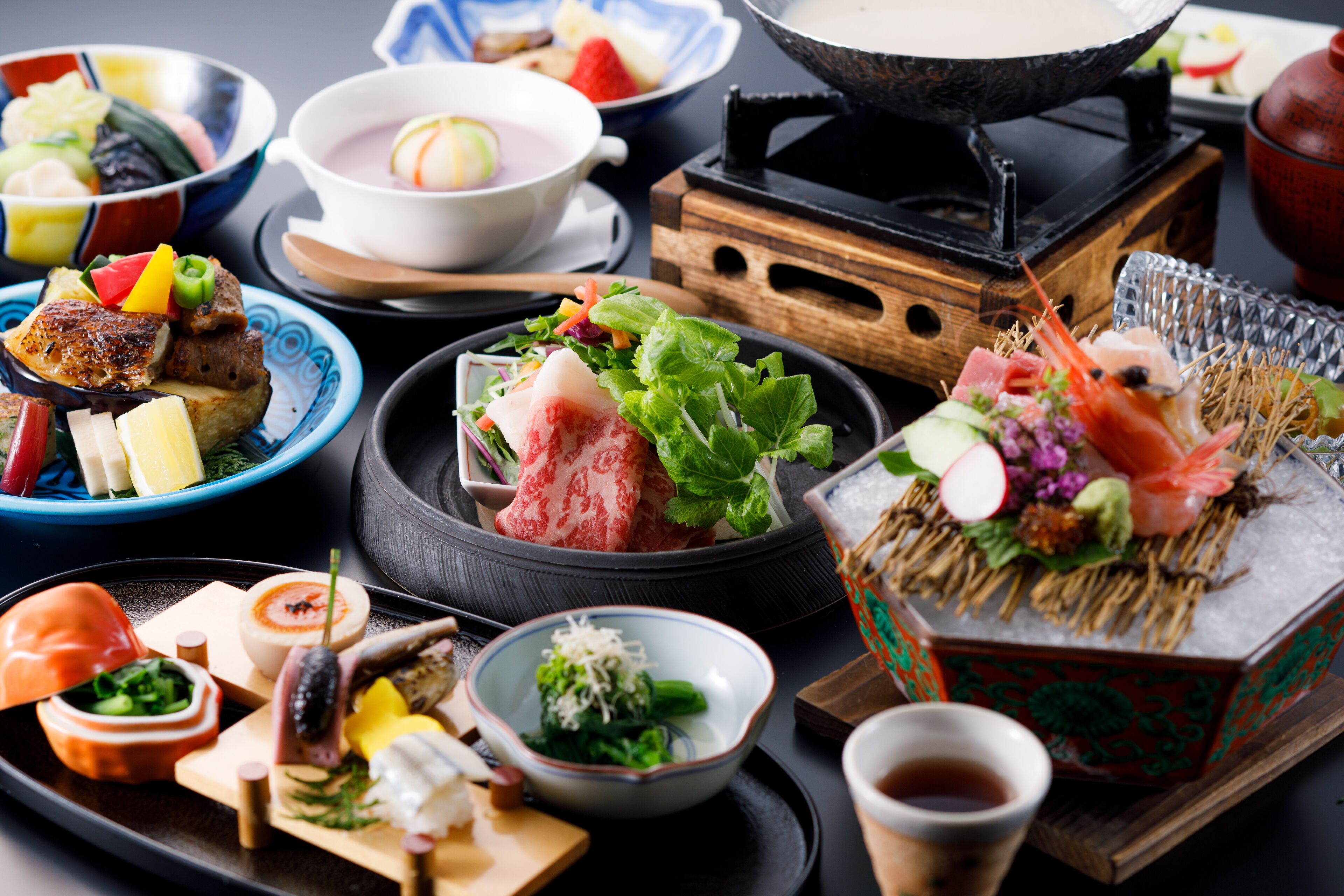 A variety of Japanese dishes, including sushi and sashimi, served on a wooden table with a hot pot and bowls.
