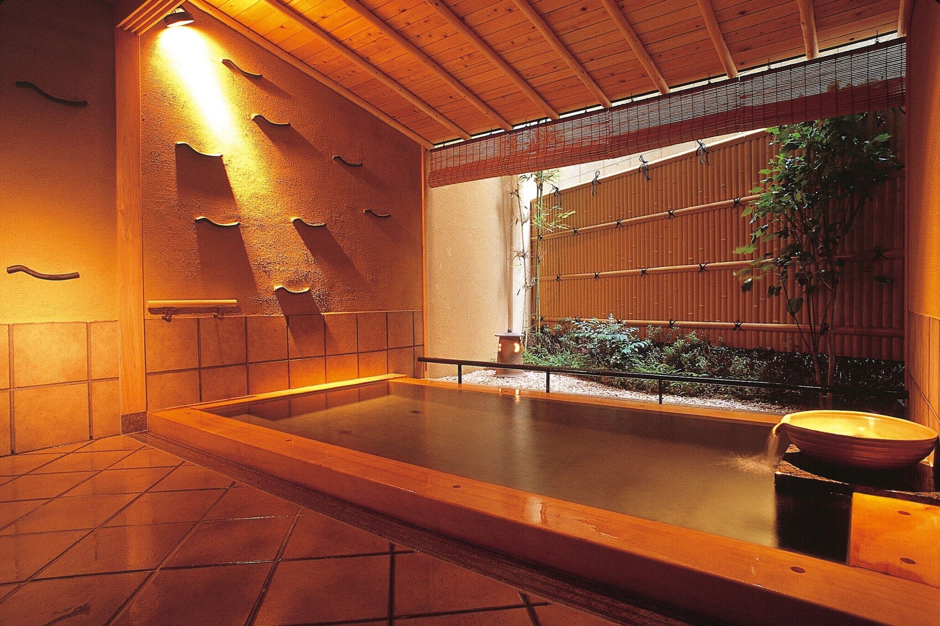 A traditional Japanese onsen with a wooden bath, tiled floor, and bamboo wall.