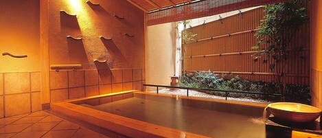 A traditional Japanese onsen with a wooden bath, tiled floor, and bamboo wall.