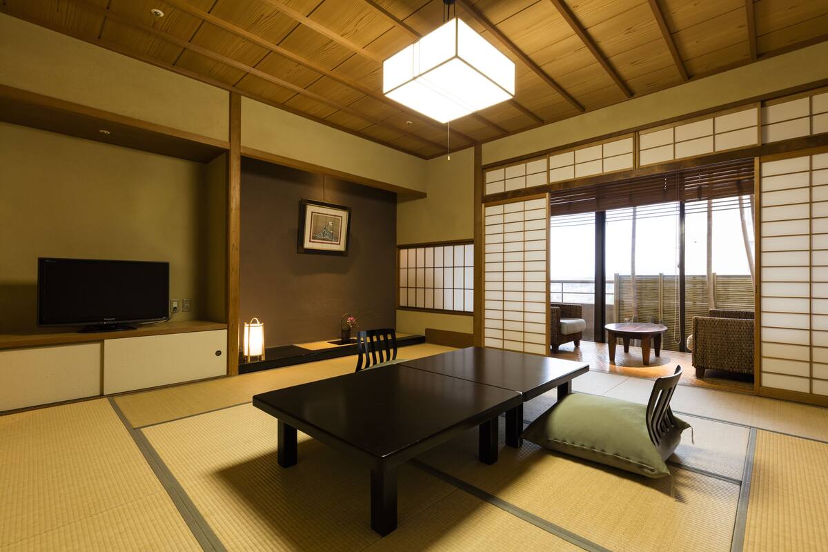 Ett traditionellt japanskt rum med tatamimattor på golvet, ett lågt bord, stolar, en tv och skjutdörrar.