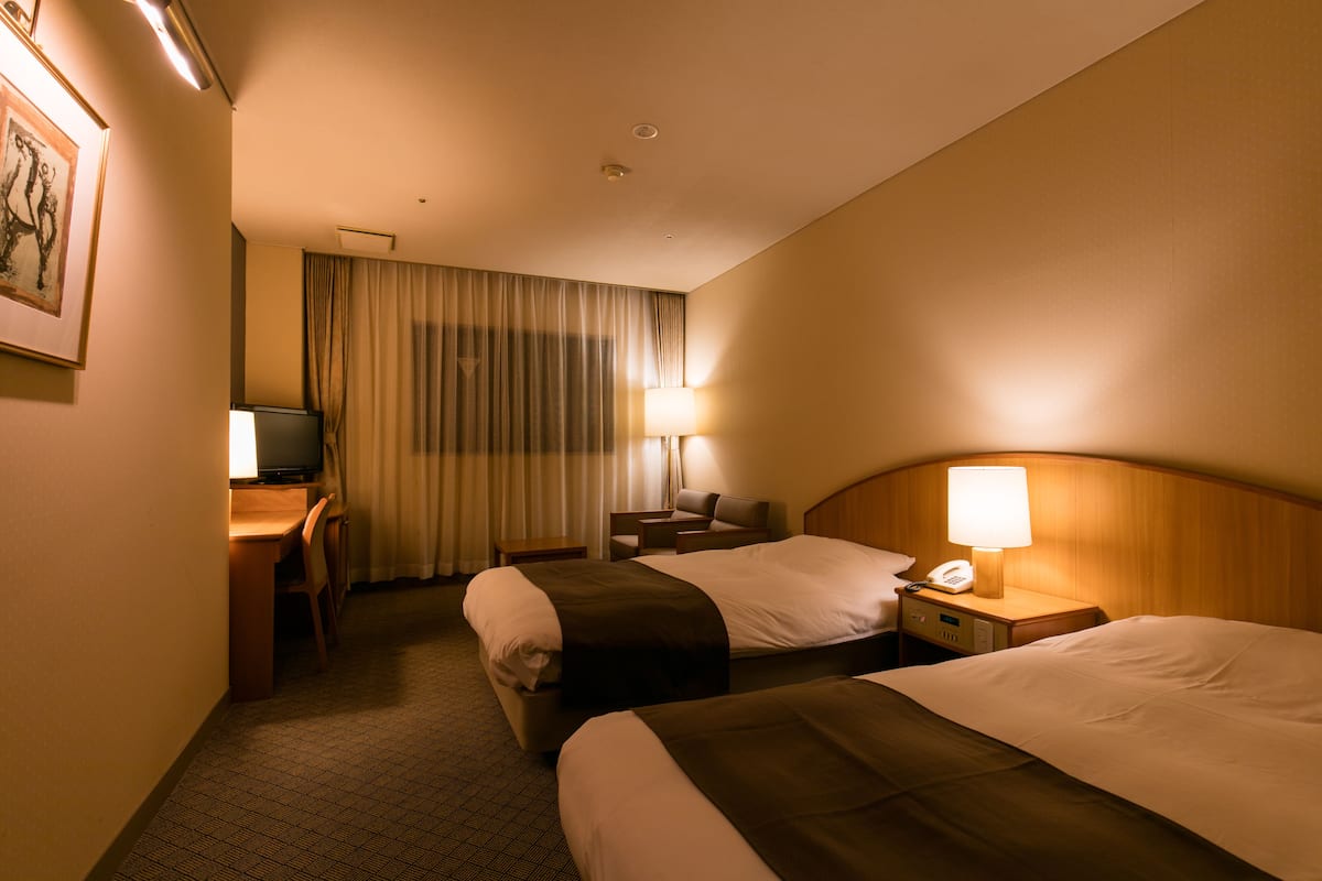 Ett hotellrum med två sängar, ett skrivbord med en stol, en tv och en lampa.