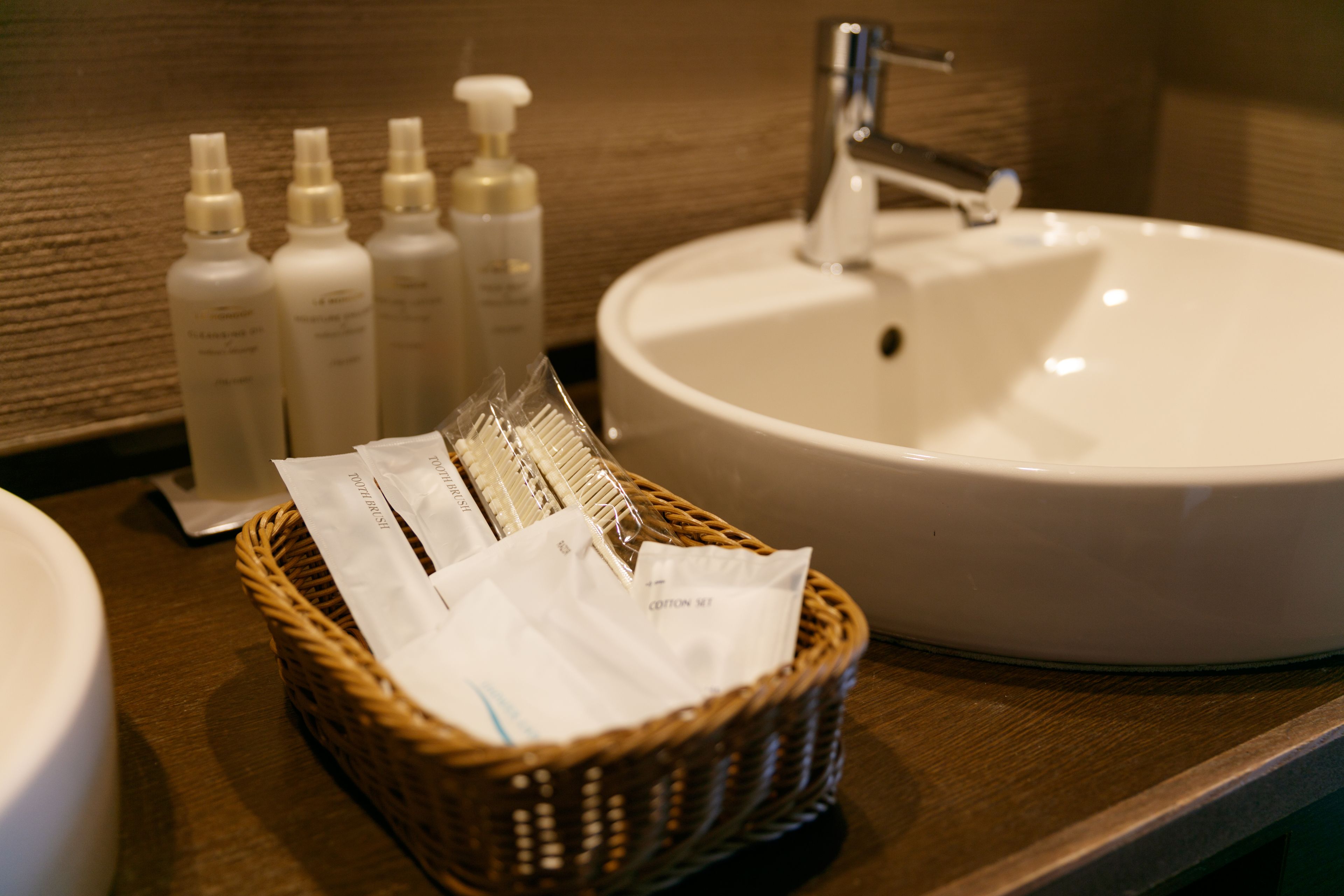 A bathroom sink with toiletries and a basket of cotton pads.