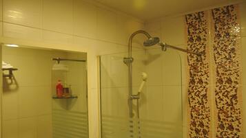 Dusche mit Glastür, Handbrause und Handtuchhalter mit Shampoo- und Conditionerflasche.